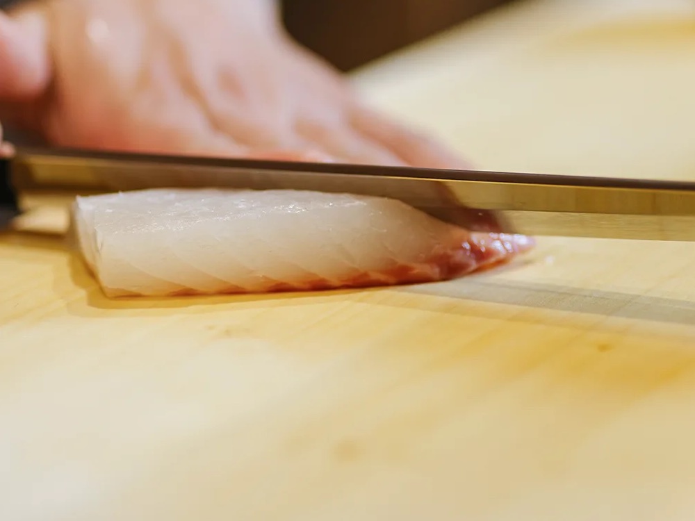 A sushi knife slicing a block of fish