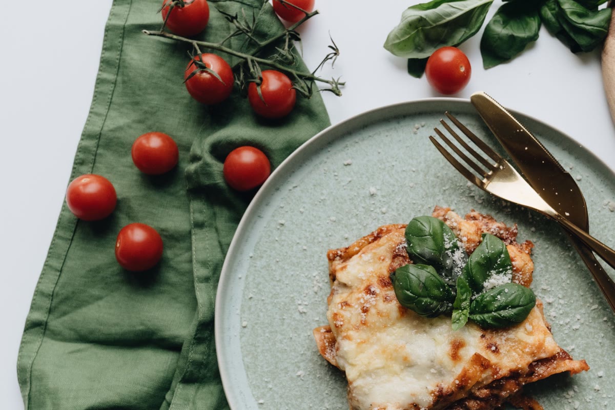 A slice of lasagna topped with basil on a green plate