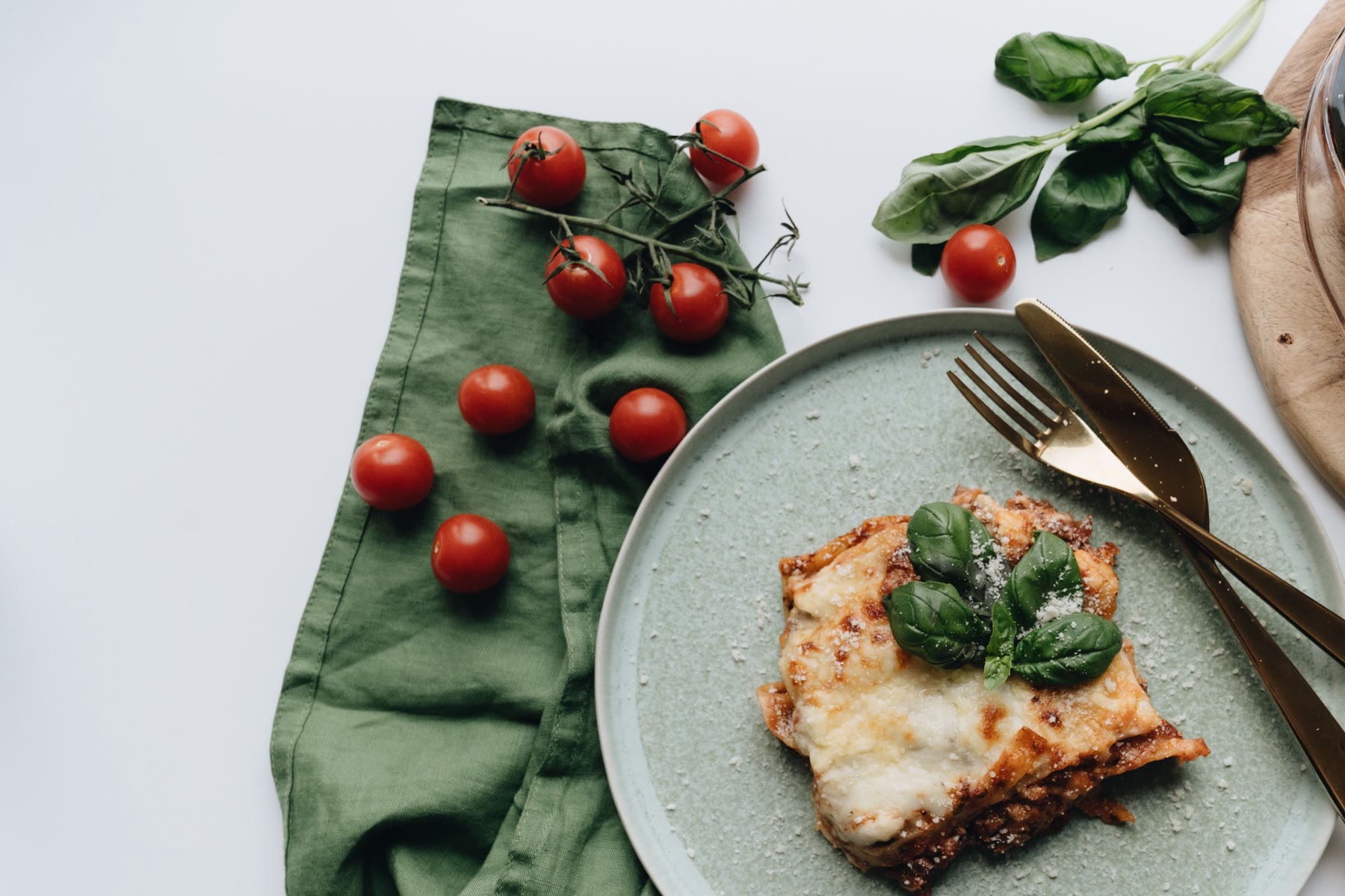 A plated slice of lasagna beside the baking dish, with cherry tomatoes and basil
