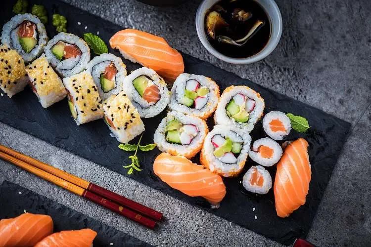 Sushi rolls, uramaki and salmon nigiri on a slate board with chopsticks