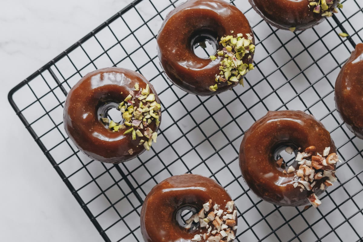 Chocolate-glazed donuts topped with chopped nuts, cooling on a wire rack