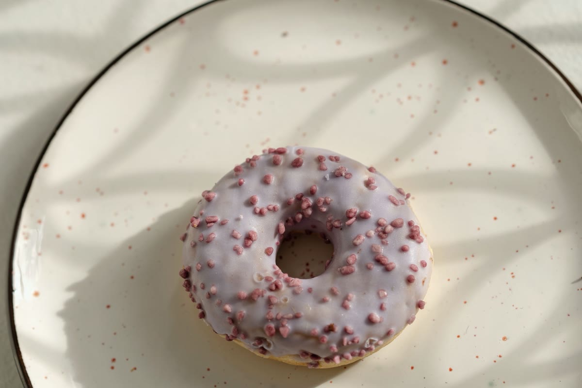 A donut with lilac glaze and pink sprinkles on a speckled plate