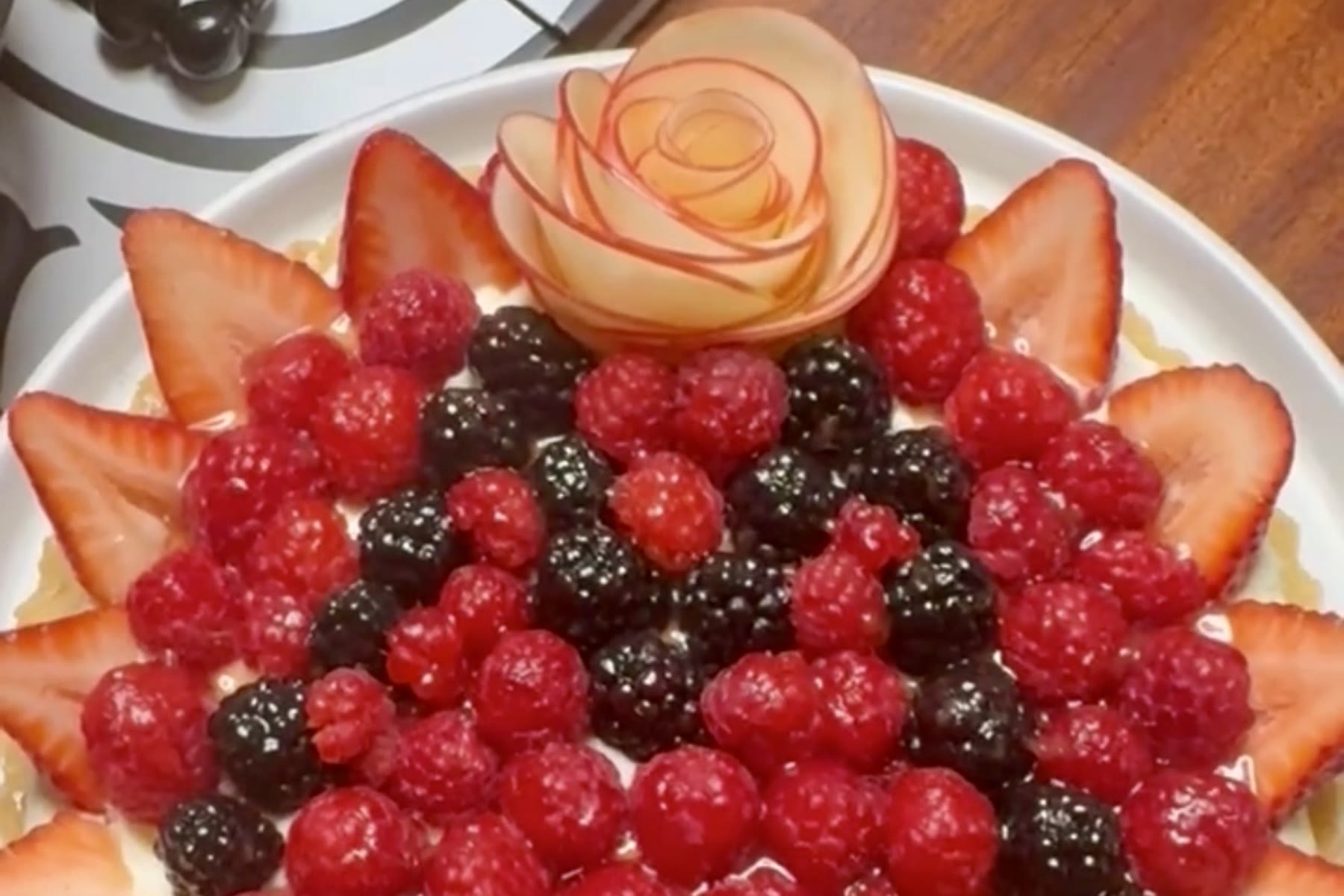 A berry tart topped with raspberries, blackberries, strawberries and an apple rose