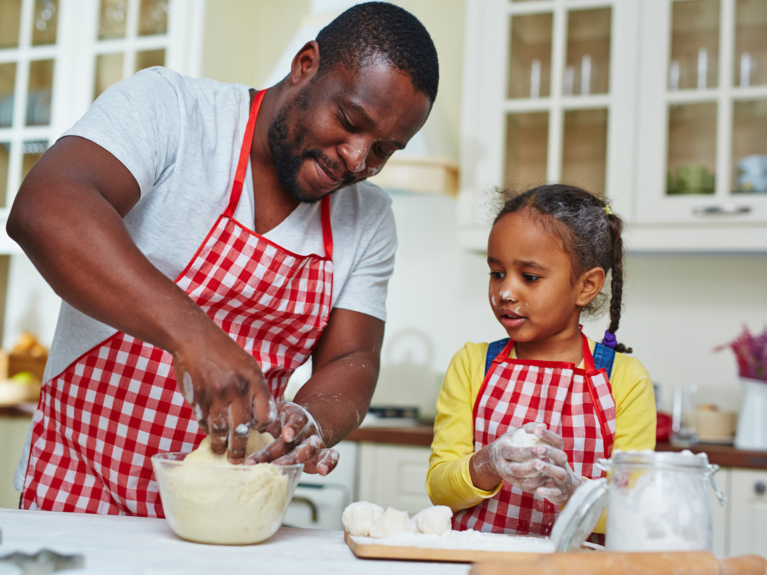 A dad and his daughter in aprons, kneading dough together